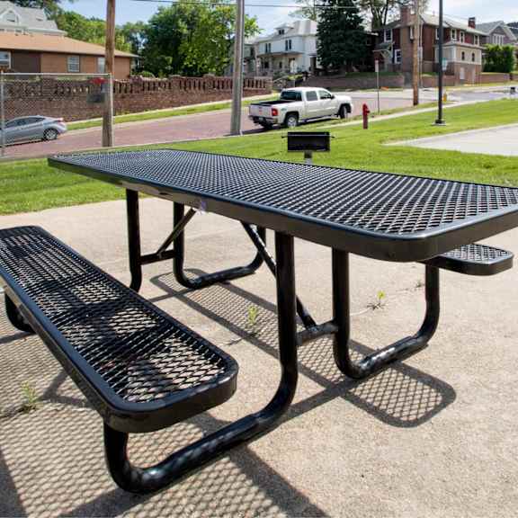a black picnic table and bench are in the foreground of a sunny day.
