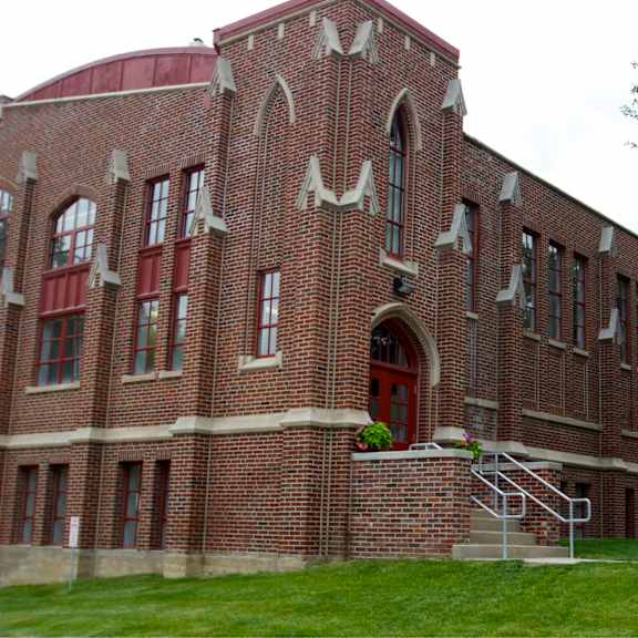 a red brick building with a large arched doorway and a staircase leading to the entrance.