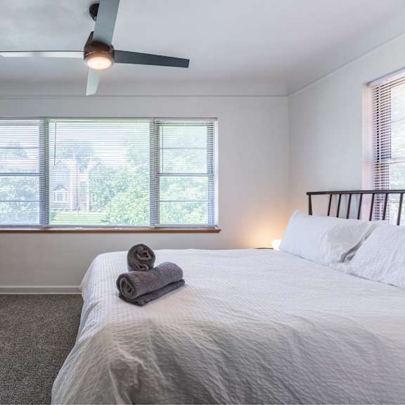 a bedroom with a large bed, a television, and a window with a view of trees and a house.