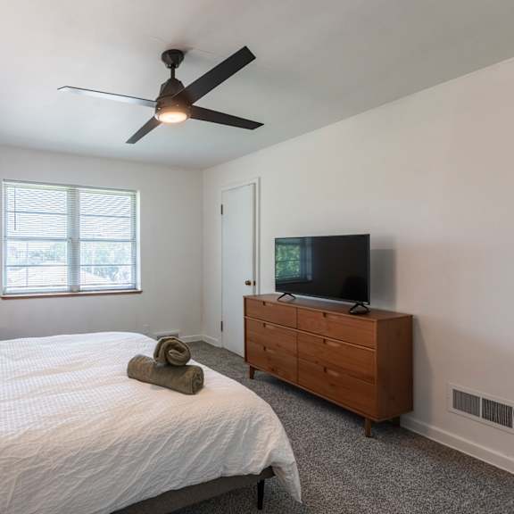 a bedroom with a bed, a ceiling fan, and a television.