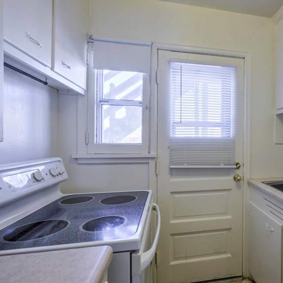 a small white kitchen with a stove, sink, and cabinets.