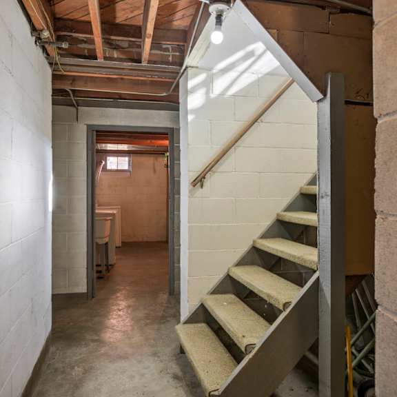 a staircase in a basement with a concrete wall on the left and a wooden beam on the ceiling.