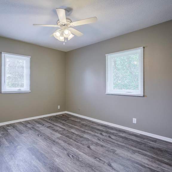 a room with a ceiling fan and two windows.