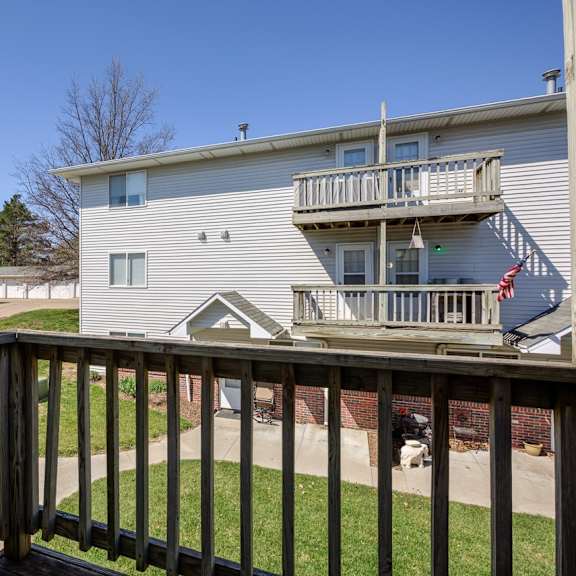 a wooden deck overlooks a grassy area and a two-story building.