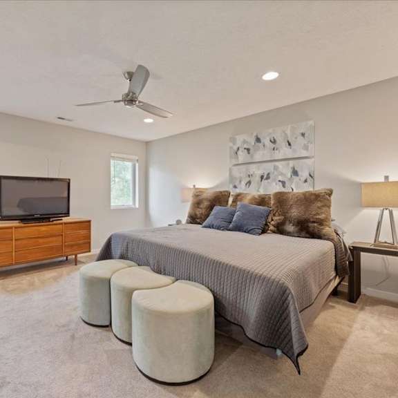 a bedroom with a bed, a dresser, a television, and a ceiling fan.