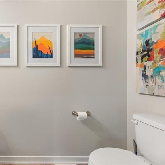 three framed artworks hang on a wall above a white sink.