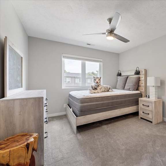 a bedroom with a bed, nightstand, and a window with a dog on the windowsill.