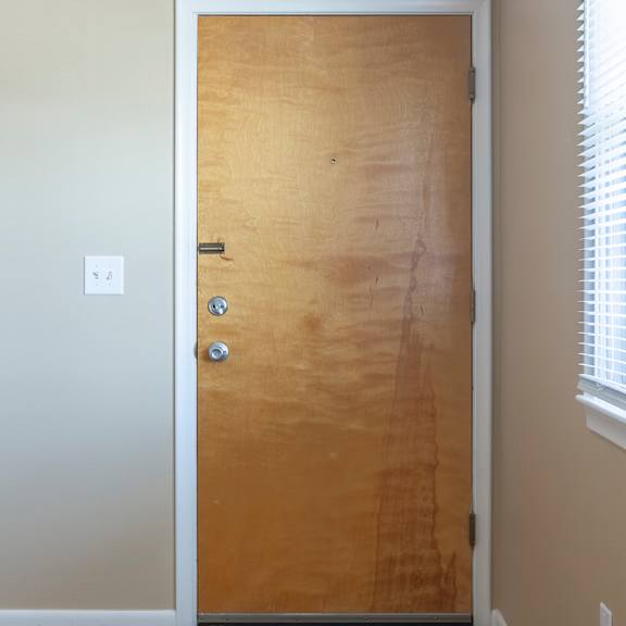 a brown door with a silver handle and a round white thing on the ceiling.