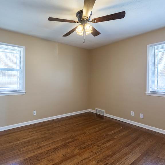 a room with a ceiling fan and two windows.