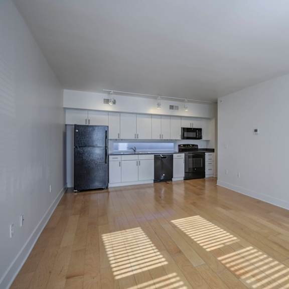 a kitchen with white walls and wooden floors with sunlight shining through the window.
