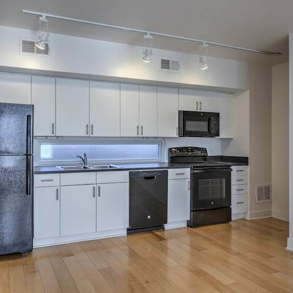 a kitchen with a black fridge, white cabinets, and wooden floors.