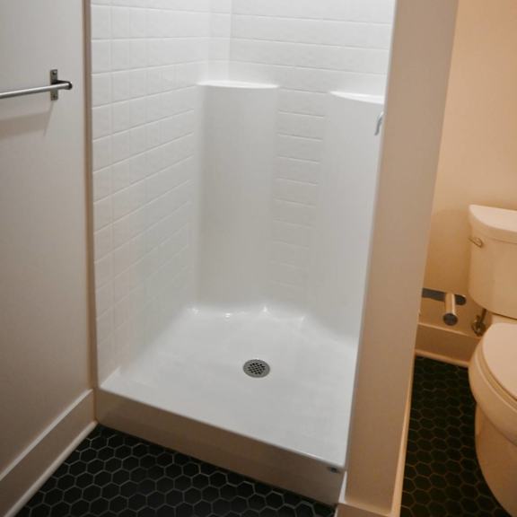 a white tiled shower stall with a drain in the middle.