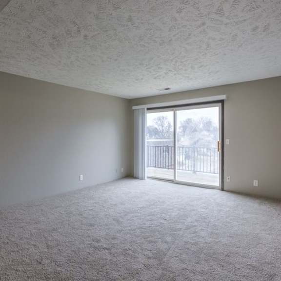 a room with a carpeted floor and a sliding glass door leading to a balcony.