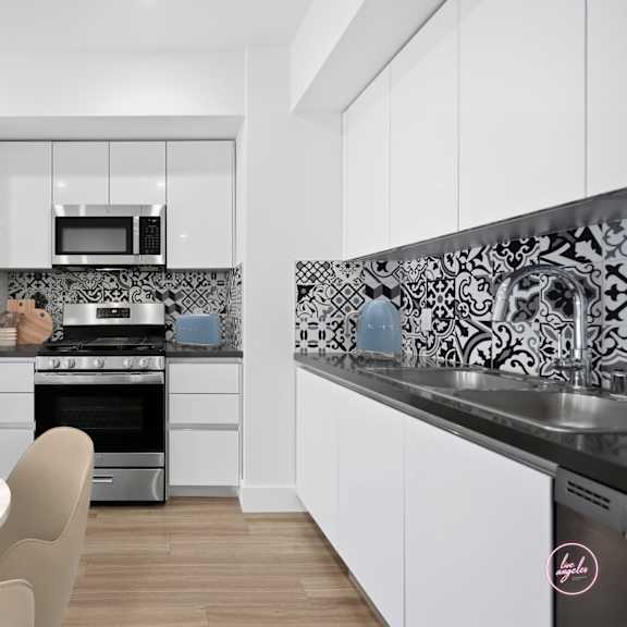 a modern kitchen with a white table and chairs, a black and white tiled backsplash, and a stainless steel refrigerator.