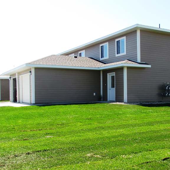 a grey house with a brown roof and a green lawn in front.