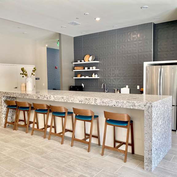 a community clubhouse kitchen with a long bar, a refrigerator, a sink, and six barstools.