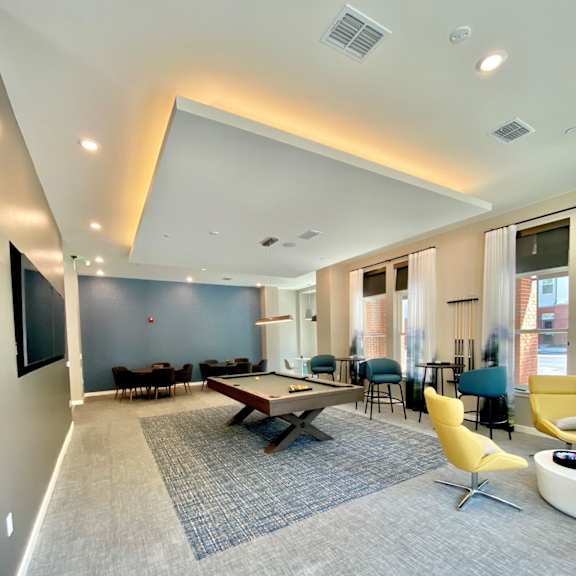 a community game room with several windows, a billiards table and seating areas with chairs and tables.