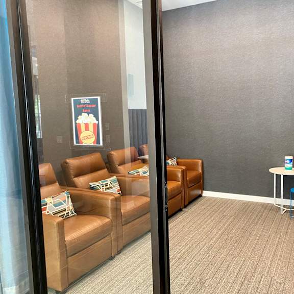 a community media room with 4 movie-theater style chairs and pillows in front of a large tv and tv console.