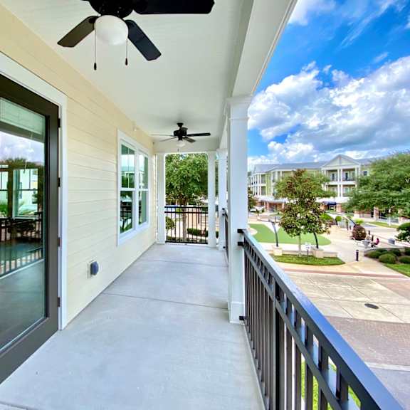 a large covered outdoor apartment balcony with two ceiling fans, and beautiful views of trees, grass, and the community.