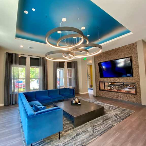 a clubhouse lobby with large windows, a comfortable l-shaped sofa, a large tv, and modern circular chandelier lighting.
