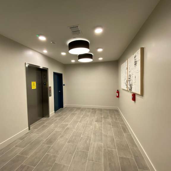 a hallway leading to a waiting area with elevators, wall art, tile-style flooring, and modern circular lights.