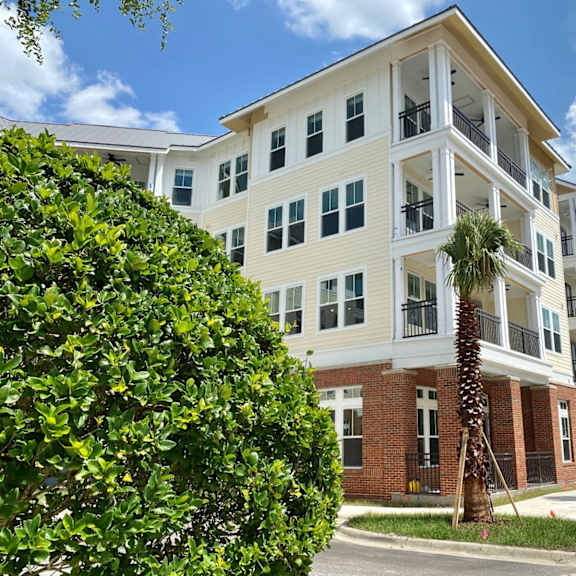exterior view of flats at tioga town center 4-story apartment building near a sidewalk with palm trees and resident parking.