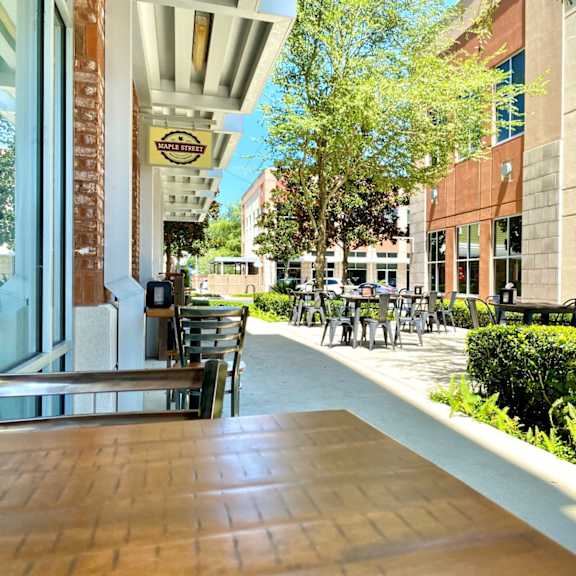 an outdoor dining area with chairs and tables in front of a local business near trees and bushes at the tioga town center.