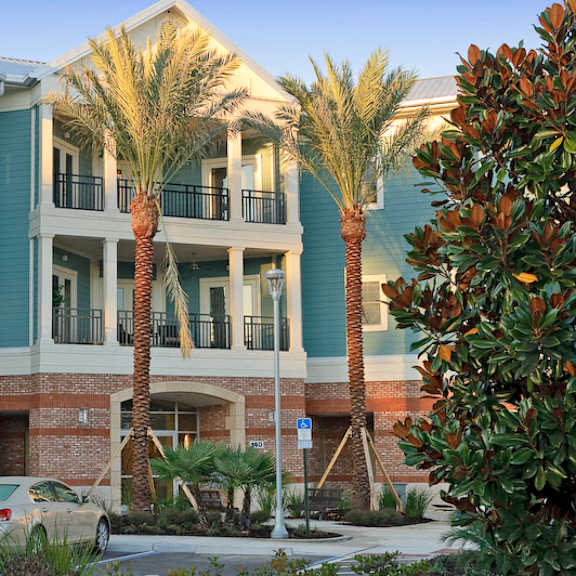 an exterior view of a 3-story apartment building at the flats at tioga town center with patios or balconies and well-maintained palm trees near resident parking.