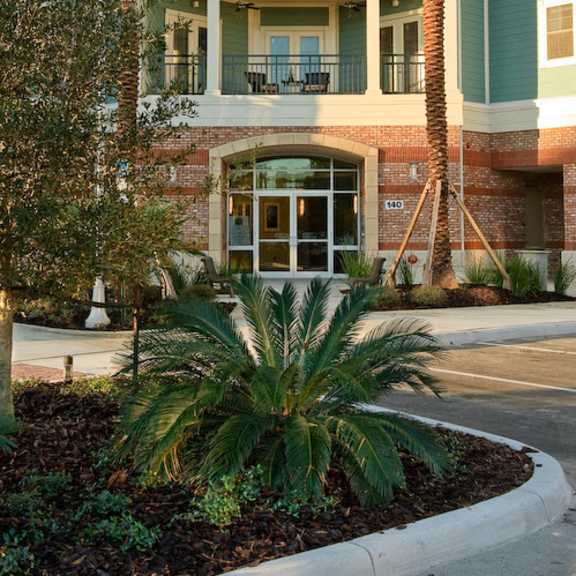 an exterior view of a 3-story apartment building at the flats at tioga town center with patios or balconies and well-maintained palm trees near resident parking.