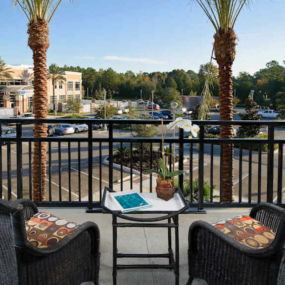 a beautiful private covered balcony with two wicker chairs and a small table with beautiful views of tioga town center, ample parking, and large trees.
