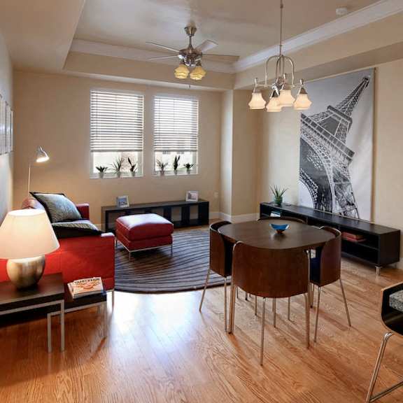 a living room with two windows, a ceiling fan, and hardwood-style flooring near a bedroom and open access to a kitchen.