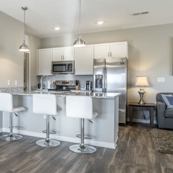 Thumbnail 10 of 23 A modern kitchen with white bar stools and a wooden floor.