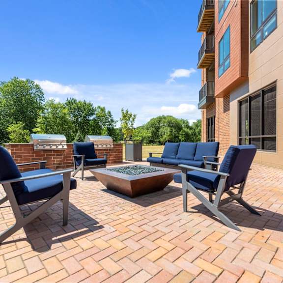 an outdoor community patio with a firepit lounge and two barbecue grills near grass and large trees. at keva flats, exton, 19341