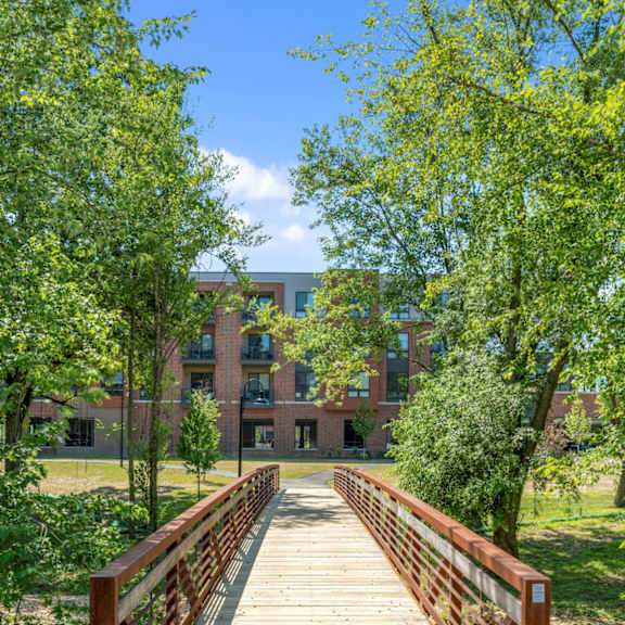 a wooden footbridge over a running creek with large trees at keva flats apartments in exton, pa