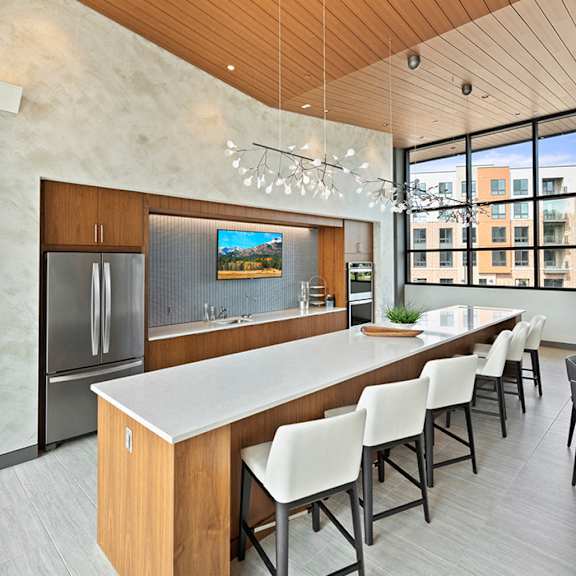 a community kitchen with a long quartz island, bar stool seating, a sink, refrigerator, a large window, and modern pendant chandeliers. at keva flats, exton, pa