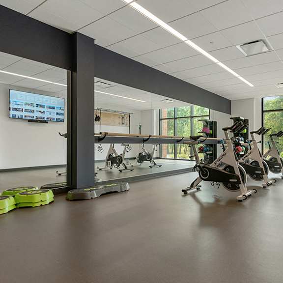 a state-of-the-art fitness center with a row of cardio bicycles, a large mirror, and panoramic windows with views of green space. at keva flats, exton, pa, 19341