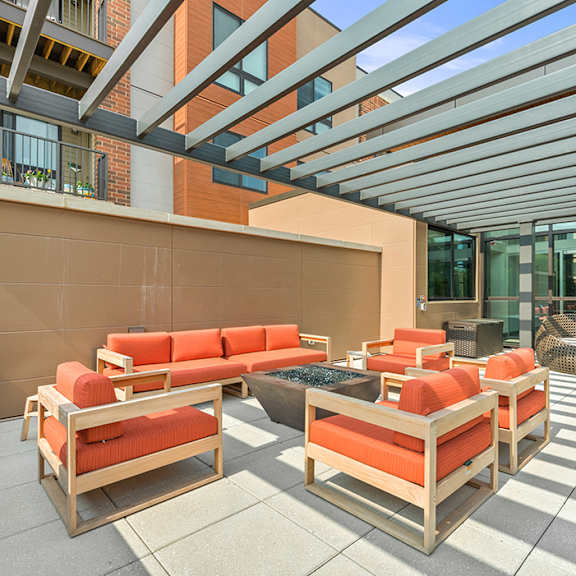 an outdoor patio with a fire pit, comfortable seating, large tile flooring, and artificial turf under a pergola. at keva flats, exton, 19341