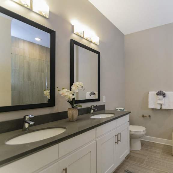 a bathroom with two sink vanities, quartz countertops, two mirrors, a toilet, modern tile flooring, and a stand-up shower. at keva flats, exton, pa