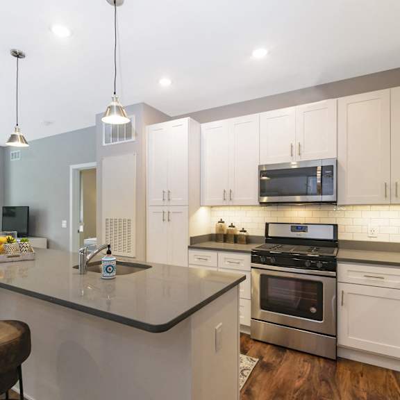 a modern kitchen with pendant and recessed lighting, a kitchen island, stainless steel appliances, and hardwood-style flooring near the living room. at keva flats, exton, 19341