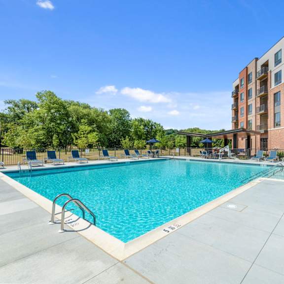 an l-shaped resort-style swimming pool with a sun deck, grills, lounge chairs, fire pits, and games at new kent's exton, pa apartment building. at keva flats, exton, pennsylvania