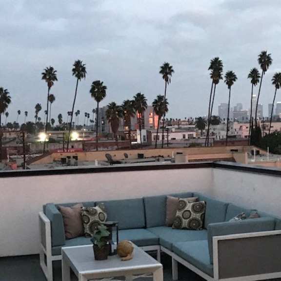 a patio with a couch, table and a view of palm trees and buildings.