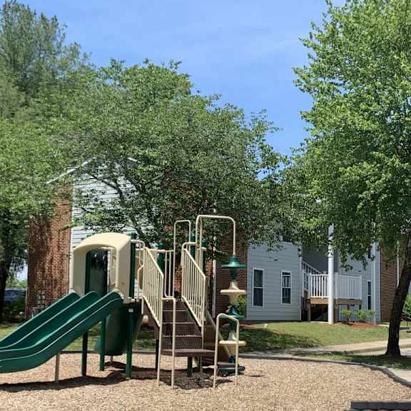 a playground with a slide and playset in front of a house