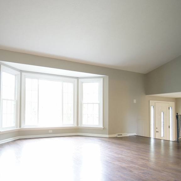 a large room with a floor to ceiling window and hardwood floors a doorway leading to another room.