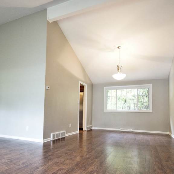 a room with wooden floors and a window with a view of trees and a staircase to the left leading upstairs..