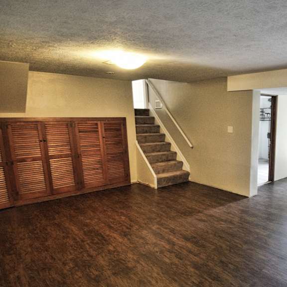 a room with wooden floors and a staircase leading to upstairs and a patio door that leads to outside.