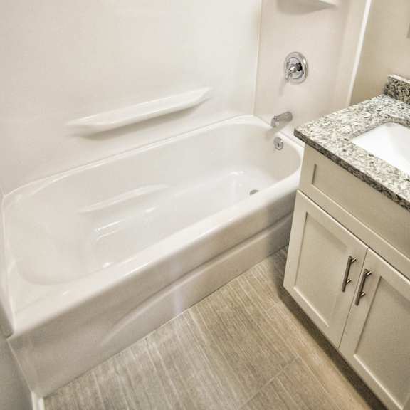a white bathtub with a shower head and a sink with a granite countertop..