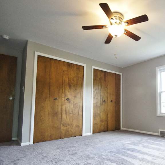 a room two closets with wooden doors and a ceiling fan and a window.