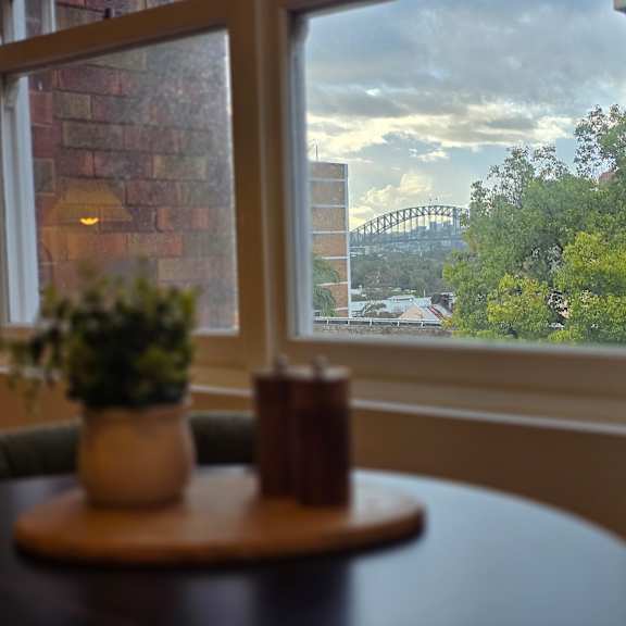 a table with a plant and candle on it in front of a window with a view of a bridge and trees.