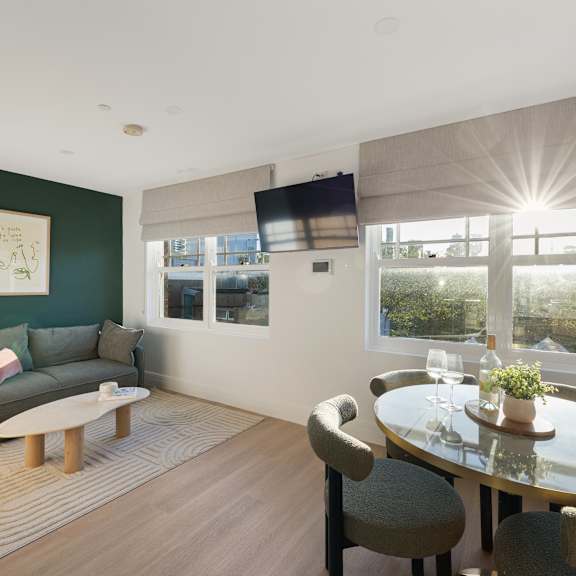 a living room with a grey couch, a glass table, and a television mounted on the wall.