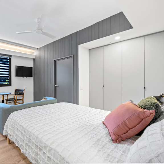a bedroom with a bed, a chair, a table, and a tv mounted on the wall.